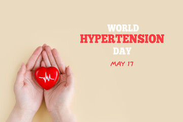 World Hypertension Day. Women's hands hold red heart with heartbeat chart - a symbol of high blood...