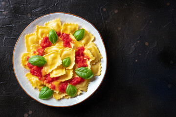 Fototapeta na wymiar Ravioli with tomato sauce and fresh basil leaves, overhead shot with a place for text. Italian recipe on a black slate background