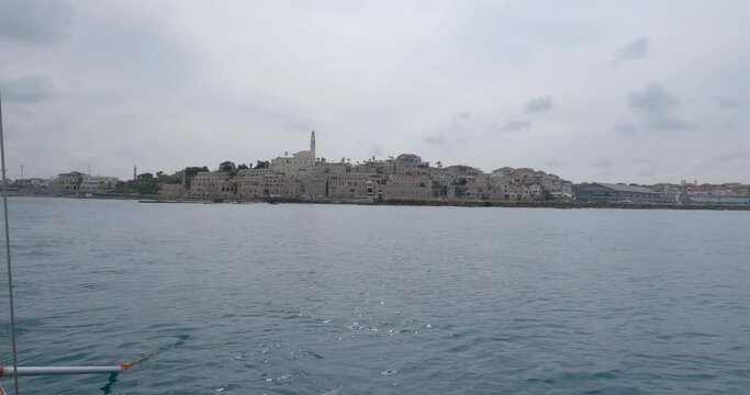 A view from the sea of the old city architecture buildings. A rowboat sailed in front of a harbor of the port of Old Jaffa. High quality 4k footage