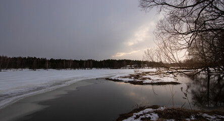 Flood. March evening by the river, the snow is melting. Evening in early spring. Trees are reflected in the water.