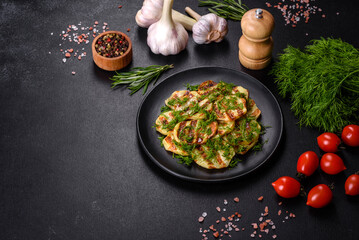 Delicious grilled potato slices with spices and herbs on a black plate