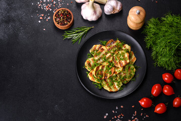 Delicious grilled potato slices with spices and herbs on a black plate