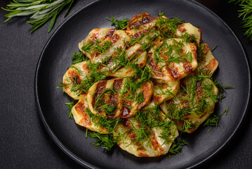 Delicious grilled potato slices with spices and herbs on a black plate