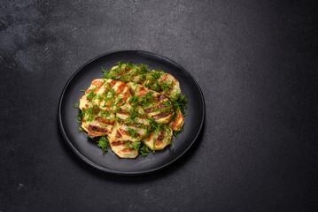 Delicious grilled potato slices with spices and herbs on a black plate