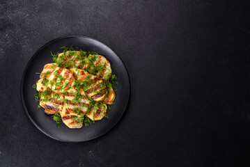 Delicious grilled potato slices with spices and herbs on a black plate