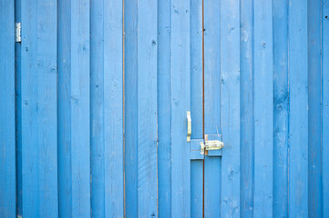 Wooden gate made of boards painted blue, closed with a latch. Copy space.
