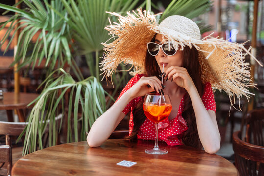 Relaxed young woman in sunglasses with aperol spritz drink on tropical background