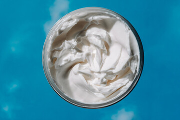 Jar with moisturizing cream on the reflections of blue skies