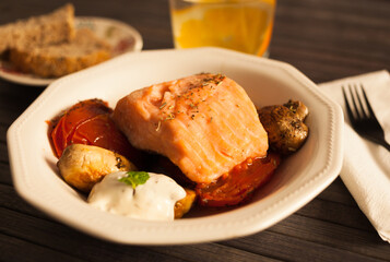 steamed sea trout fillet served on fried mushrooms with tomatoes in a white bowl