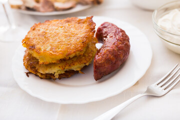 Fried grated potato pancakes with fried sausage on white plate