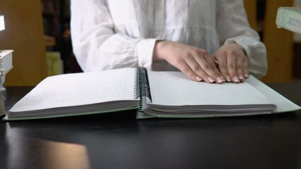 Blind girl reading a text of Braille in library. Hand touches the description in Braille.