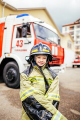 Child, cute boy, dressed in fire fighers cloths in a fire station with fire truck, childs dreamed...
