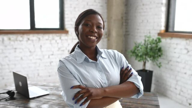 High-skilled African-American businesswoman wearing smart casual shirt stands with arms crossed in modern office space. Multiracial bossy lady, purposeful leader, female entrepreneur