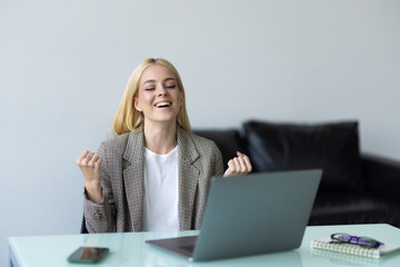 Happy young woman excited with great news, win, success, luck. Woman looking at laptop screen making winner gesture, shouting fir joy, laughing, celebrating achieve, good result, promotion