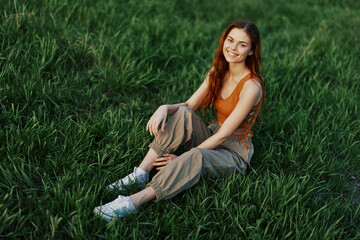 Lifestyle summer women on vacation in the park sitting on the green grass looking at the camera and smiling