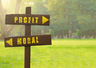 Wooden signs Profit versus Moral on a natural green background copy space.