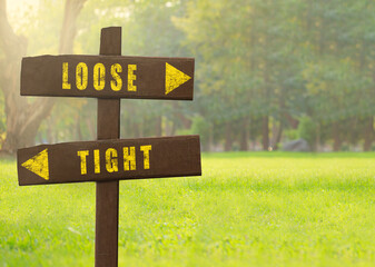 Wooden signs Loose versus Tight on a natural green background copy space.