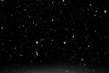 Real falling white snow against black night sky above snowy ground in the winter. Snowing at dark.