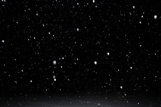 Real Falling White Snow Against Black Night Sky Above Snowy Ground In The Winter. Snowing At Dark.