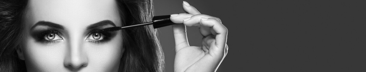 Woman with beautiful make-up is applying mascara on her lashes