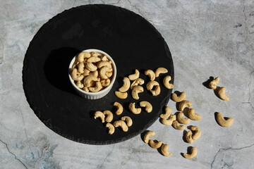 Cashew nuts on the black stone plate on the cement background. Top view.