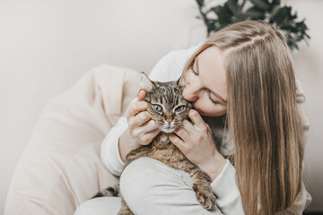 Young caucasian blonde woman hugging and kissing her brown tabby cat