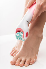 Female feet and electric foot scrubber or massage device on white background