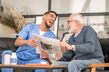 Caregiver and an aged man laughing at a news item