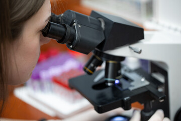 Young attractive veterinary worker in gloves using microscope for testing blood samples of animals. Vet doctor looking into microscope, close-up.