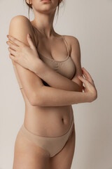 Tender beauty. Young slim woman posing in beige underwear isolated over grey studio background - obrazy, fototapety, plakaty