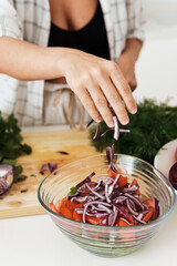 Female hands cooking vegetarian salad and adding red onion to it