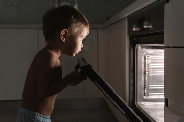 Curious baby boy opens the hot oven. Concept of safety and possible problems with unattended...