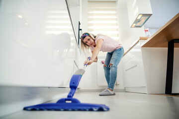 Tidy woman sweeping kitchen floor at home with mop and detergent.