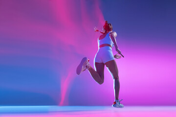 Fototapeta na wymiar Back view. Professional female athlete running away isolated on blue studio background in mixed pink neon light. Healthy lifestyle, sport, motion and action concept.