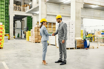 Businesspeople stand in the company's warehouse and shake hands.