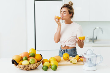 Beautiful woman sniffing fresh orange during citrus juice preparation at home