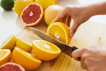 Female hands with knife slicing citrus fruits on cutting board for homemade fresh juice