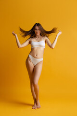 Beautiful woman with slim figure posing in white underwear isolated over yellow studio background