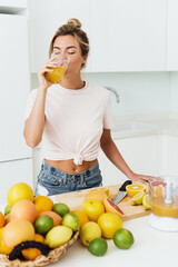 Woman drinking freshly squeezed homemade orange juice in white kitchen