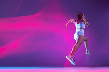 Fototapeta na wymiar back view. Professional female athlete, runner training isolated on blue studio background in mixed pink neon light.