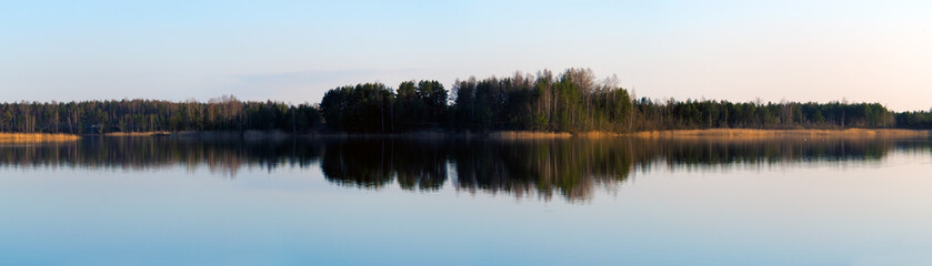 Long panorama view with lake reflecting forest on evening