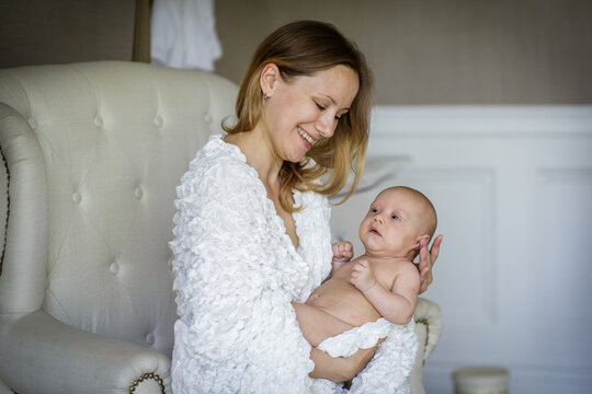 Young happy smiling woman holding baby boy sitting in armchair. Newborn son at home. Image with selective focus