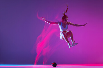 Young girl, athlete training isolated on blue studio background in mixed pink neon light. Healthy lifestyle, sport, motion and action concept.