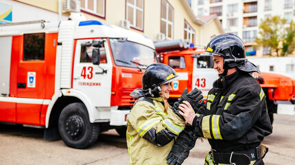 Firefighters woman and man in helmets near fire truck. Protection, rescue from danger. Fire station