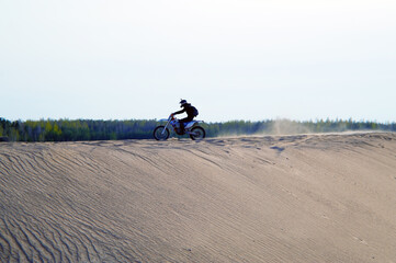 Motocross bike driving very fast on top of sand mountain straight forward
