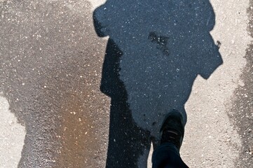 There is a foot, a puddle and a shadow on the sidewalk