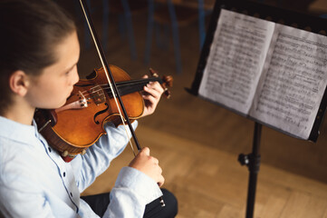 Young student of violin playing on musical notes. Teenage violinist practicing at musical school....