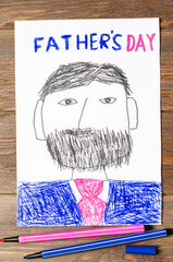 A child's drawing on a wooden table. Dad with a beard and mustache closeup. A postcard for the Father's Day holiday
