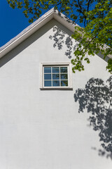 Obraz premium The white empty wall of a two-story old house with a gable roof on a sunny summer day.