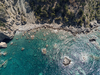 Aerial top view of sea waves hitting rocks on the beach with turquoise sea water. Sea waves on the wild rocky coast. Seascape. Travel concept. Aegean Sea, Turkey. Postcard view. Drone shot